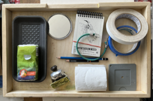 Packing for a Plein Air Trip - My wood tray with assorted stuff: Styrofoam tray for pastels in use, tissue standing in for wet wipes that I need to go buy!, compact mirror, Body Shop Hemp cream, sketchbook and pencils, bungee cord, two types of tape, viewfinder.