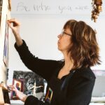 Call yourself an artist - Gail at the easel with "Be Who You Are" on wall behind her